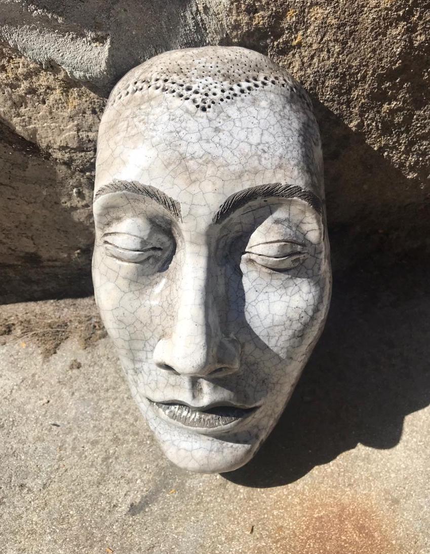 A partially cleaned raku mask resting on stone