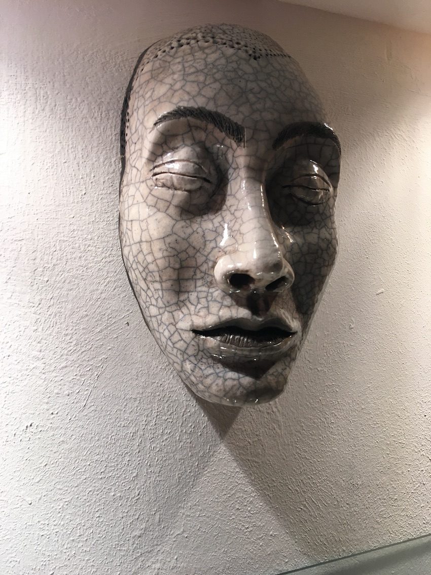 A finished raku mask with a fine crackled glaze, hanging on a wall