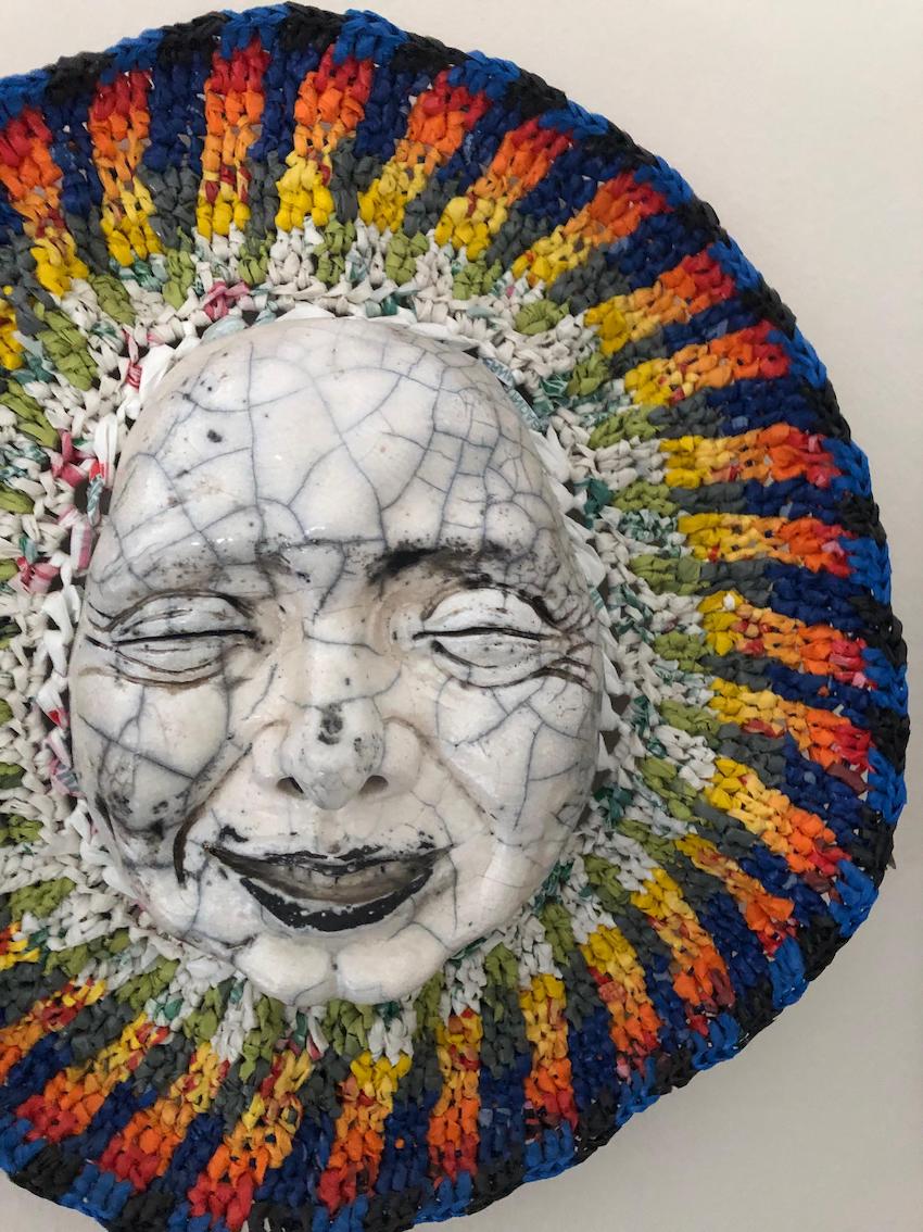 Raku-fired mask framed by a colourful headdress crafted from plastic