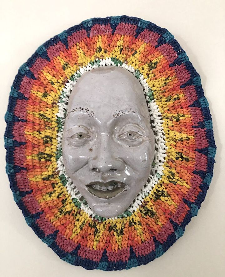 Crepuscular Bliss by Evan Oberholster — glazed ceramic face framed by a woven ring of yellow, orange and pink