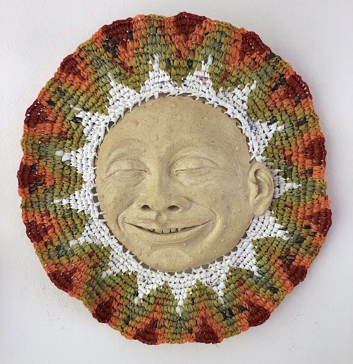 Happy Face by Evan Oberholster — smiling stone-coloured ceramic face framed by a woven ring of orange, green and white