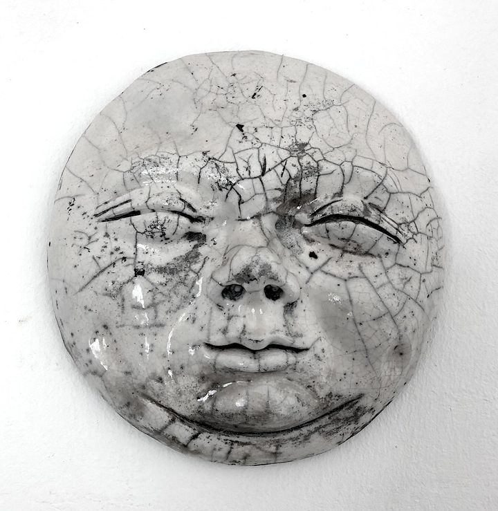 The Man in the Moon by Evan Oberholster — round raku-fired ceramic face with a crackled white glaze